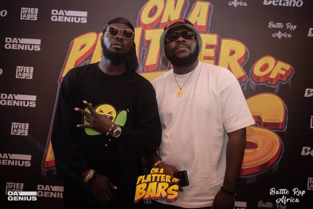 Two Nigerian battle rap artistes pose on red carpet with sponsor logos on backdrop.
